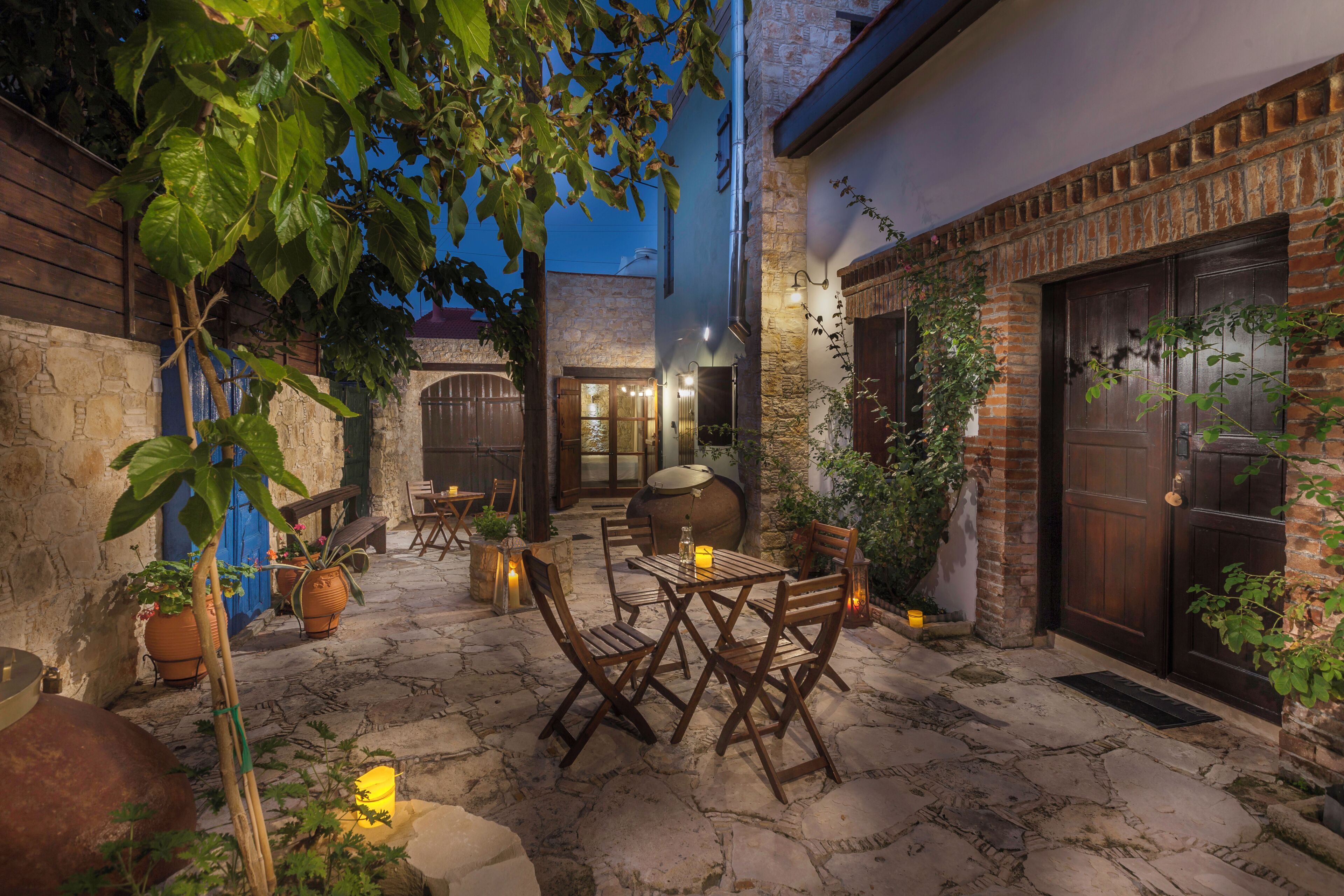 An outdoor patio with stone flooring, wooden furniture, and potted plants.