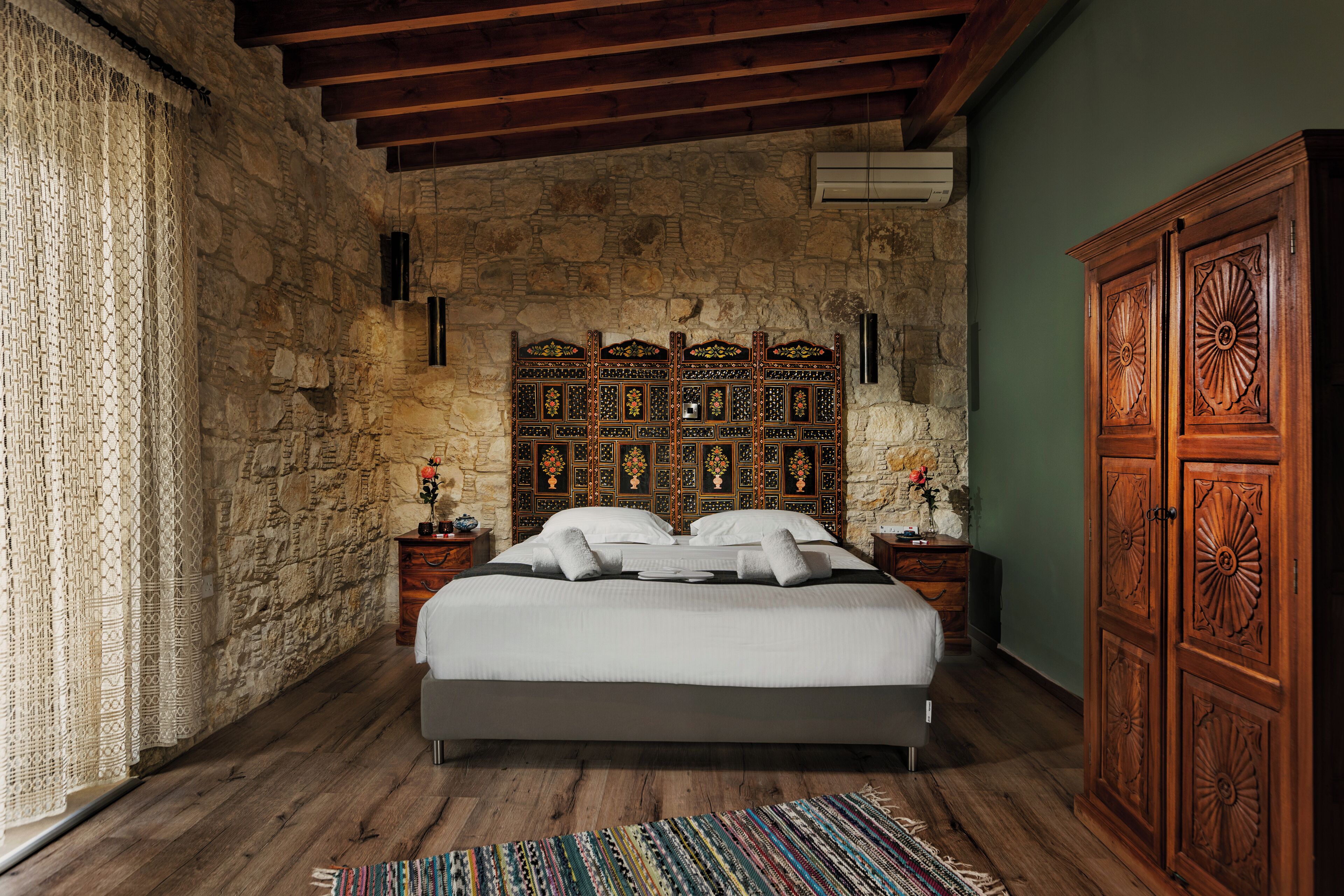 Un dormitorio con pared de piedra, cama con ropa de cama blanca, cabecero de madera y un armario grande.