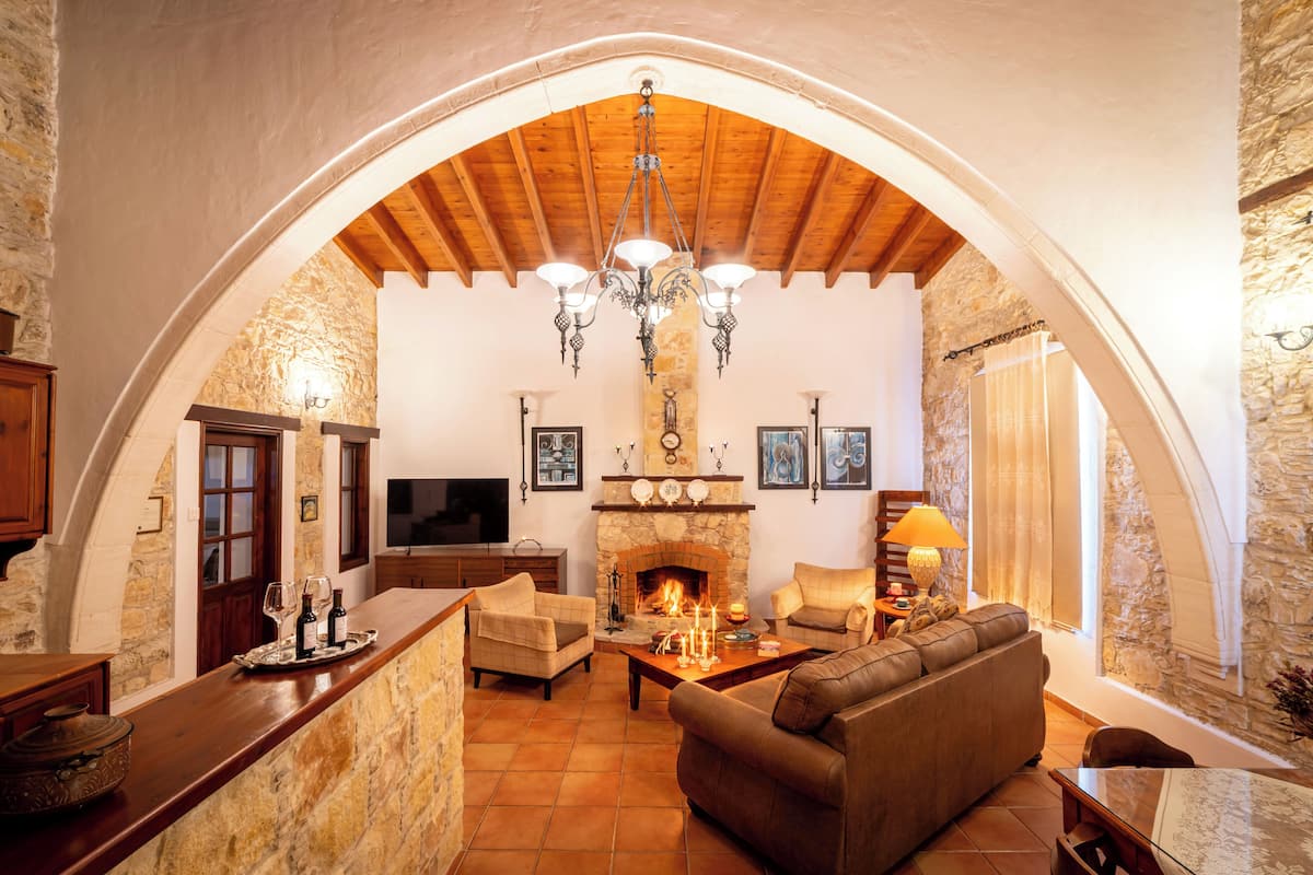 A cozy living room with a stone fireplace, wooden ceiling beams, and a television.