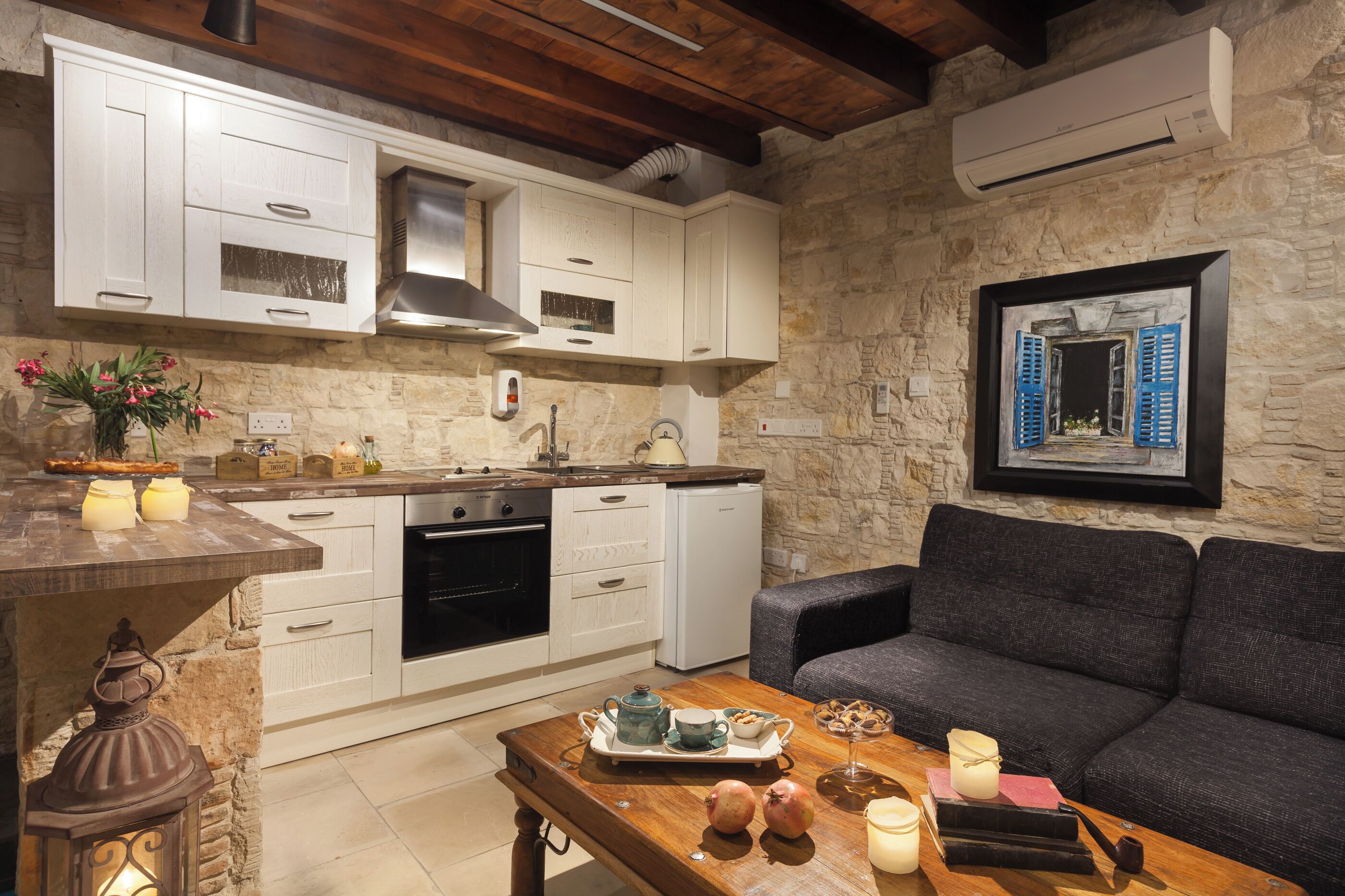 A kitchen with white cabinets, a stone wall, and a framed picture of a window.