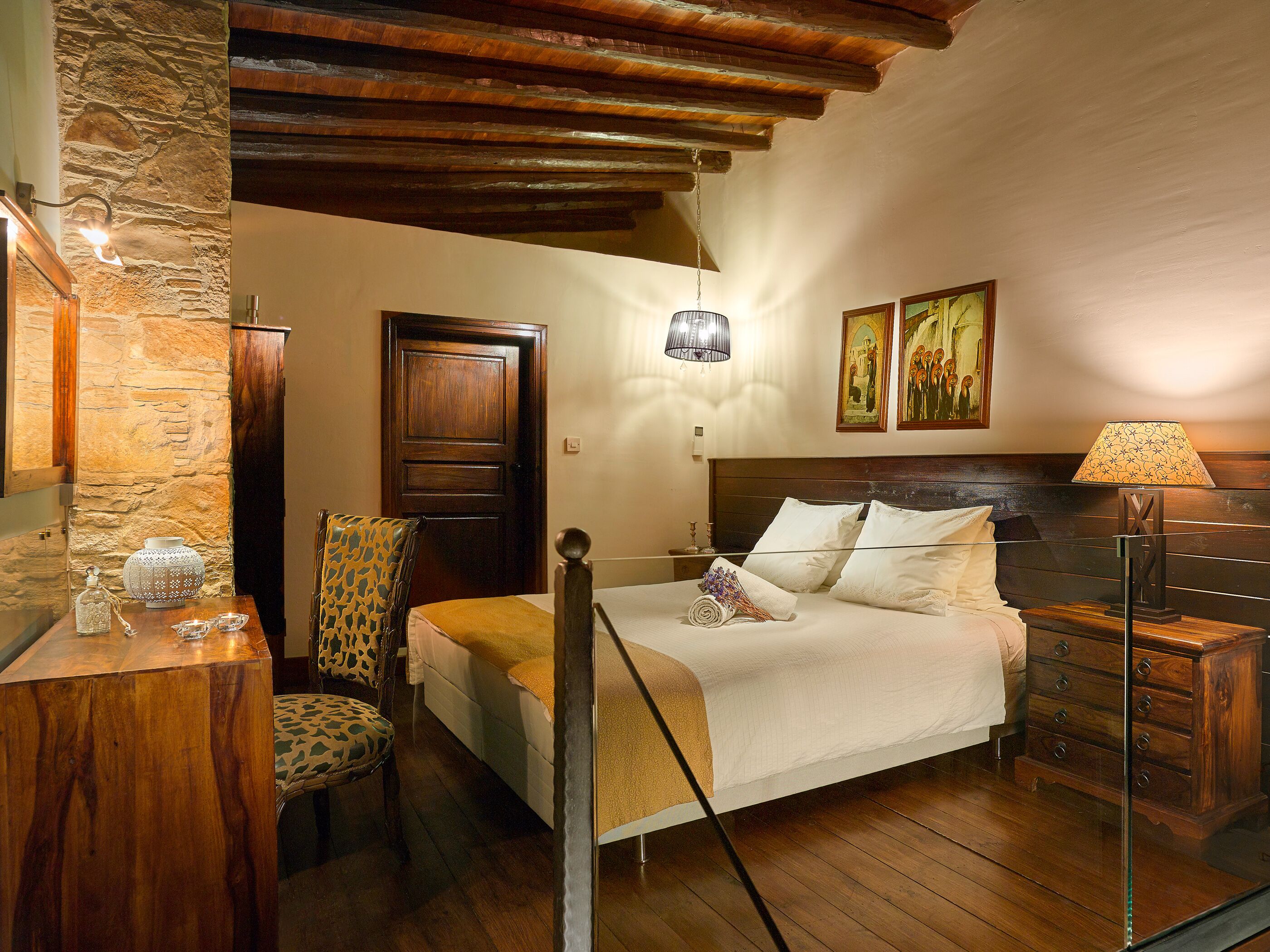 A bedroom with a wooden bed, a stone wall, a wooden ceiling, and a chandelier.