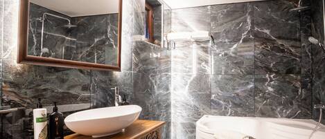 A modern bathroom with a large mirror, a wooden vanity, a white sink, a bathtub, and marble walls.