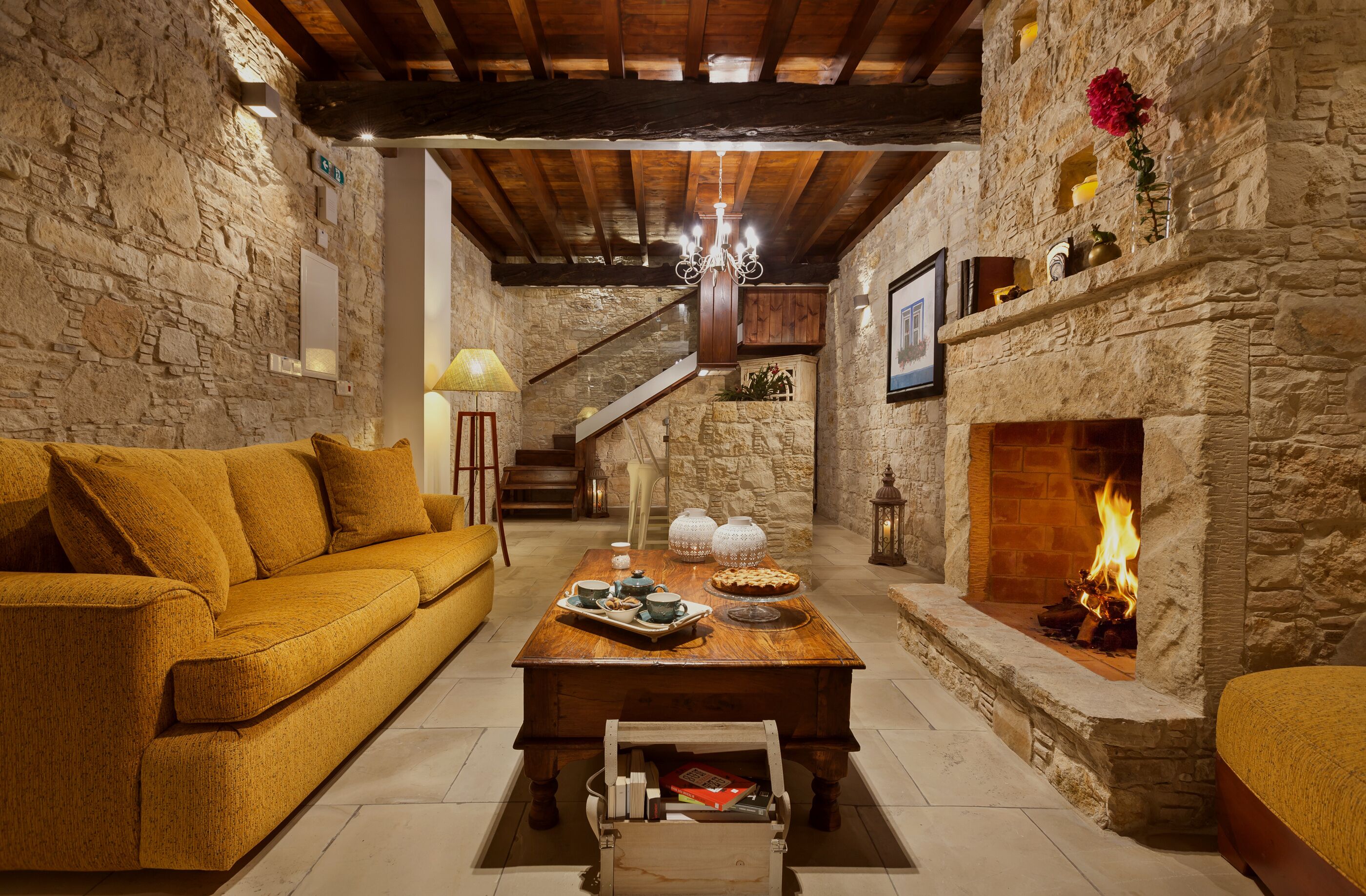 A cozy living room with a stone fireplace, a wooden staircase, and a sofa.