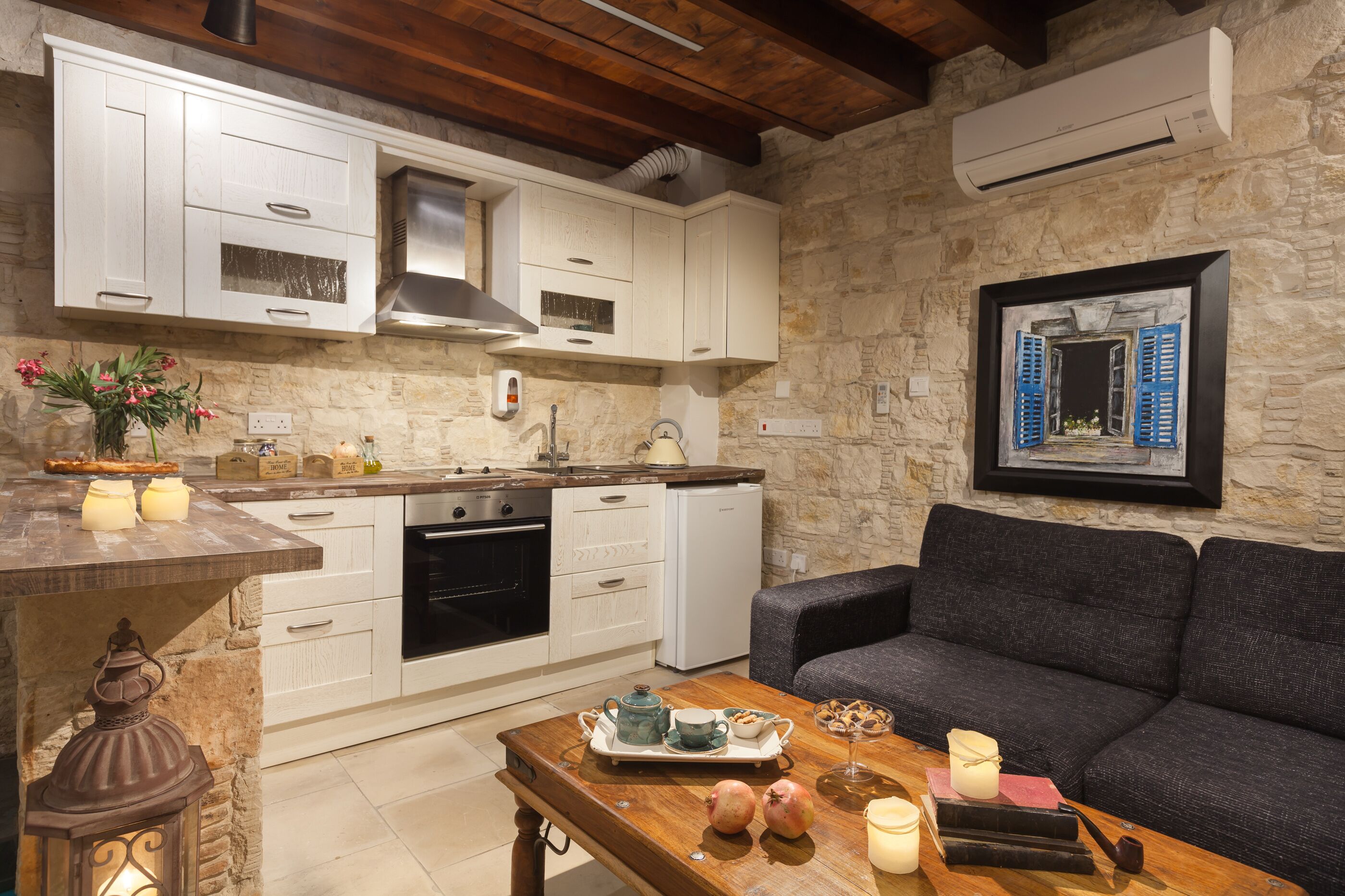 A kitchen with white cabinets, a stone wall, and a gray sofa.
