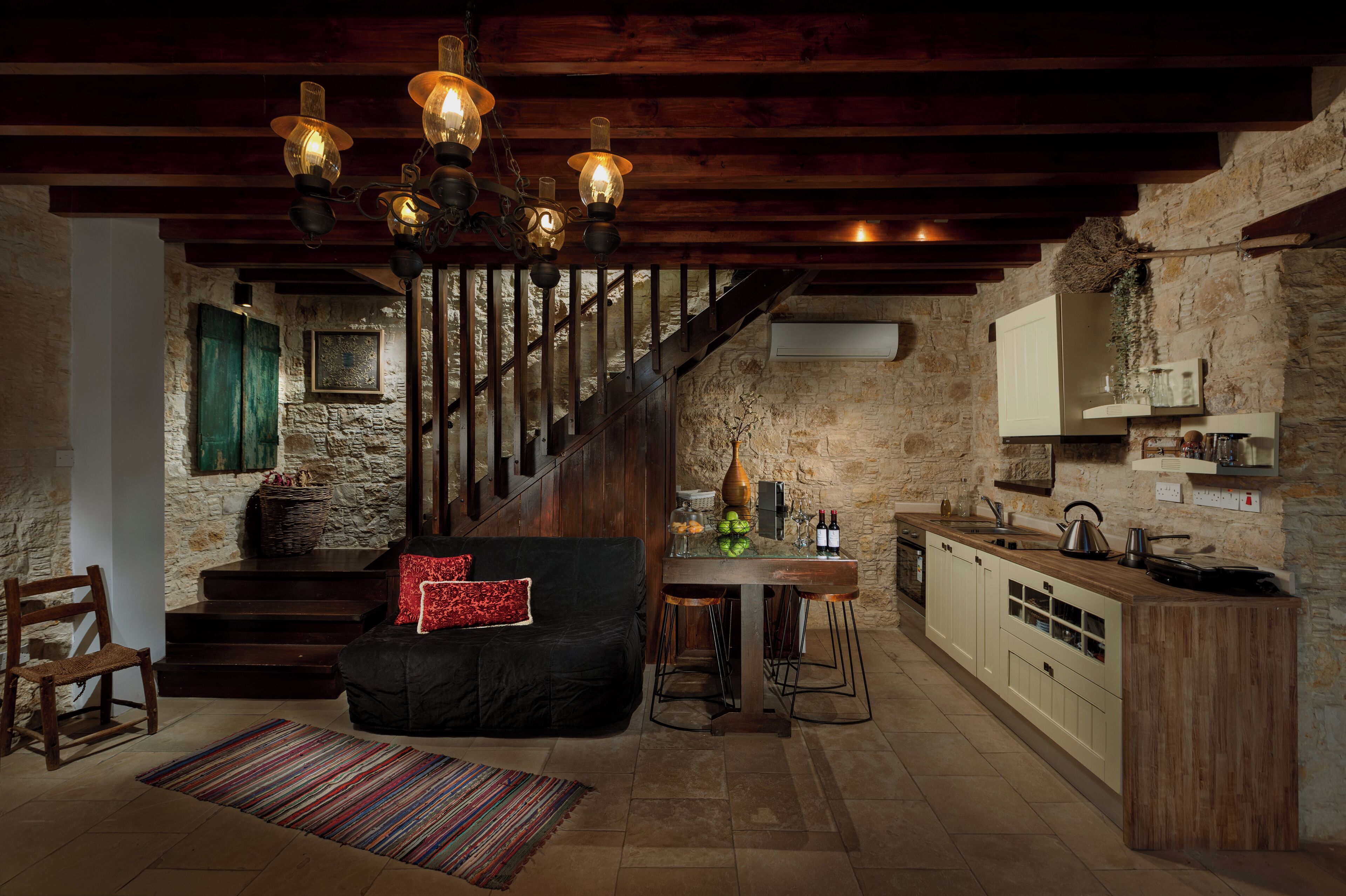 Eine rustikale Küche mit einer Holztreppe, einem schwarzen Sofa und einem Essbereich mit Hockstühlen.