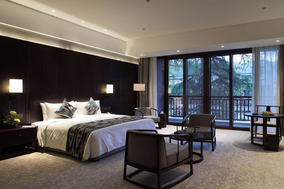 Een moderne hotelkamer met een groot bed, twee stoelen, een tafeltje en een televisie.