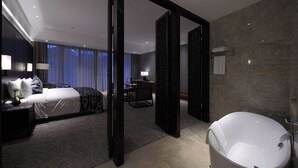 Een moderne hotelkamer met een groot bed, een zithoek, een bureau en een badkuip.