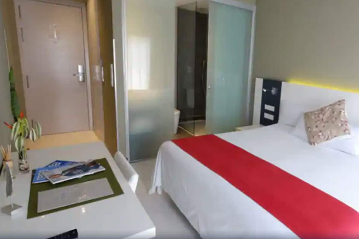 A hotel room with a bed, a desk, a chair, a door, and a mirror.
