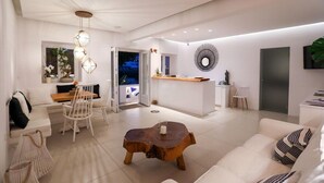 A modern living room with a white sofa, a wooden coffee table, and a dining area with a white table and chairs. - Casa Grande (Mykonos)