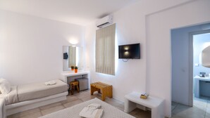 A modern hotel room with two single beds, a small wooden stool, a bench, a TV mounted on the wall, and a bathroom visible through an open door. - Casa Grande (Mykonos)