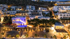 A coastal town at night with white buildings, a swimming pool, and a parking area. - Casa Grande (Mykonos)