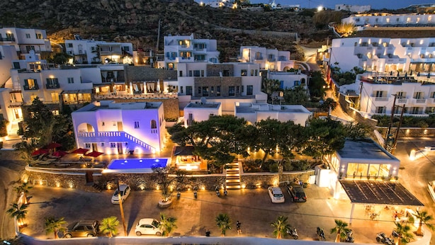 A coastal town at night with white buildings, a swimming pool, and a parking area. - Casa Grande (Mykonos)