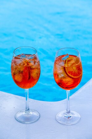 Two glasses of red beverage with ice and citrus slices, placed on a white surface with a blue background. - Casa Grande (Mykonos)