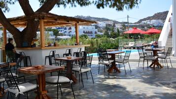 Ein Außenbereich mit Sitzgelegenheiten, einer Bar und Blick auf Pool und Gebäude im Hintergrund.