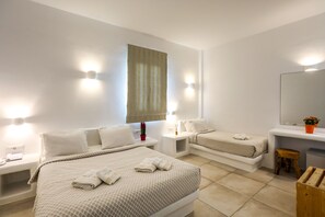 A hotel room with two beds, a small desk, a mirror, and a window with curtains. - Casa Grande (Mykonos)