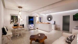 A modern living room with a white sofa, a wooden coffee table, and a dining area with a white table and chairs. - Casa Grande (Mykonos)