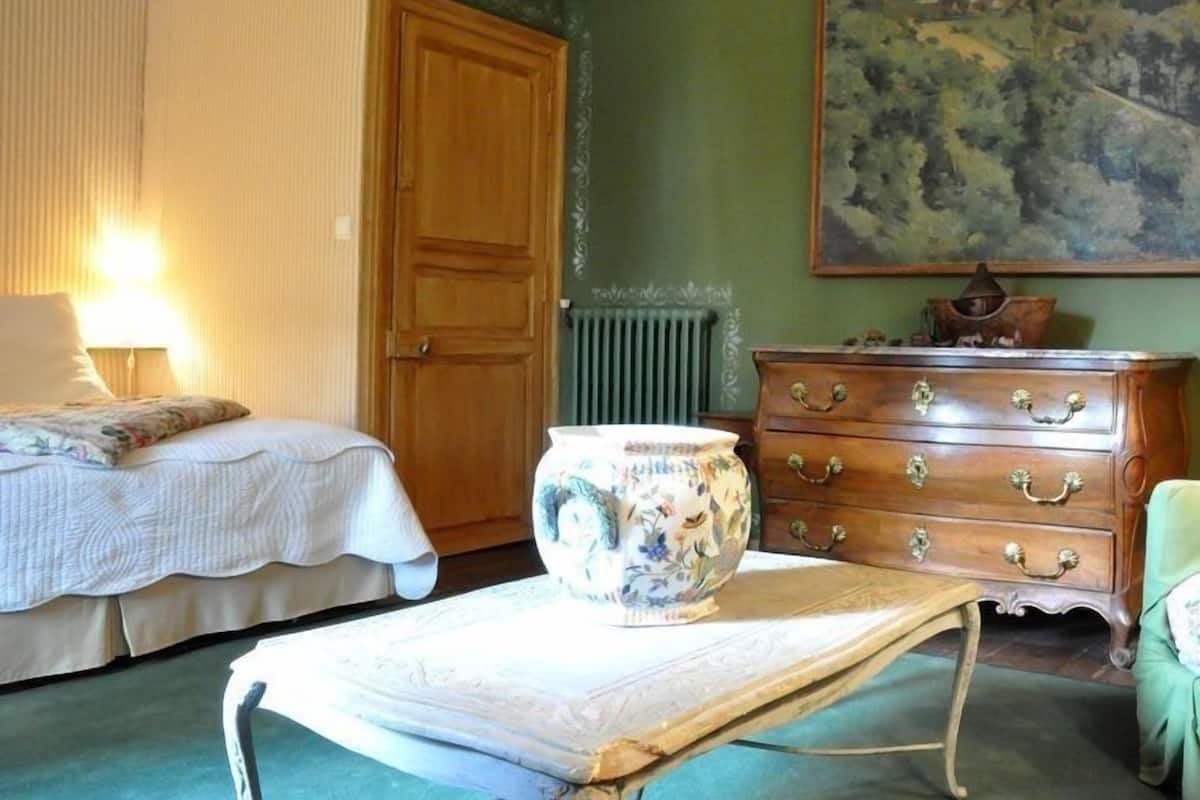 Une pièce comprenant un lit, une commode, une table avec un vase et un tableau accroché au mur.