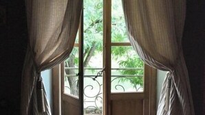 A window with sheer curtains, a metal grill, and a view of greenery outside. - La Marronnière (Cheffes)