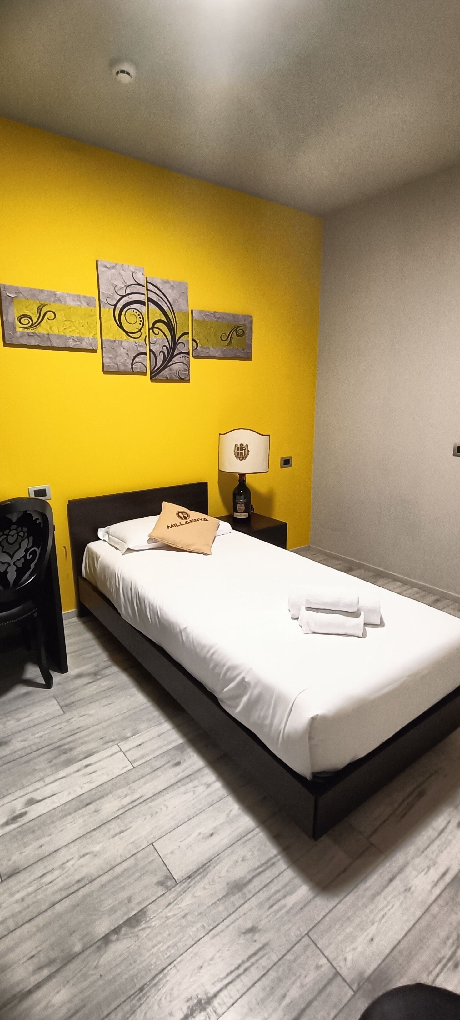 Hotelkamer met een bed, nachtkastje, lamp en wand met decoratieve panelen.