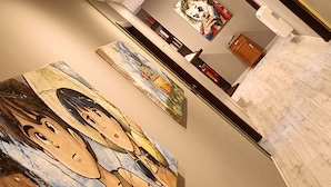 A hallway with artworks on the walls, a wooden cabinet, and a whiteboard. - Millaenya Inn (Entratico)