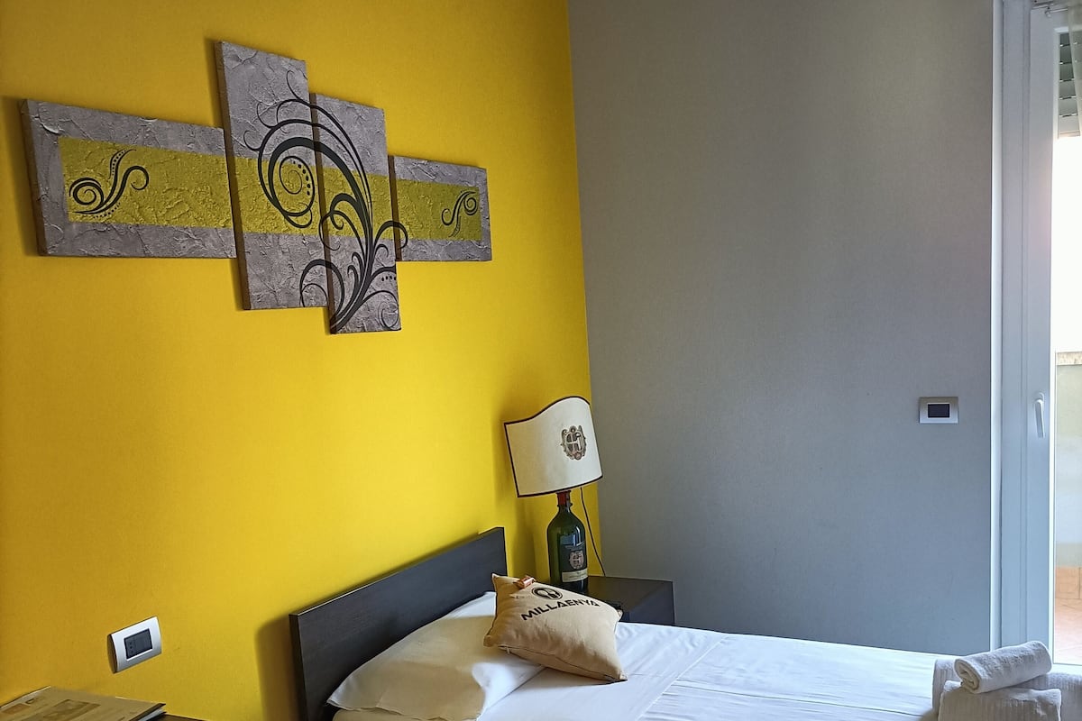 A bedroom with a bed, a bedside table, a lamp, and artwork on the wall.