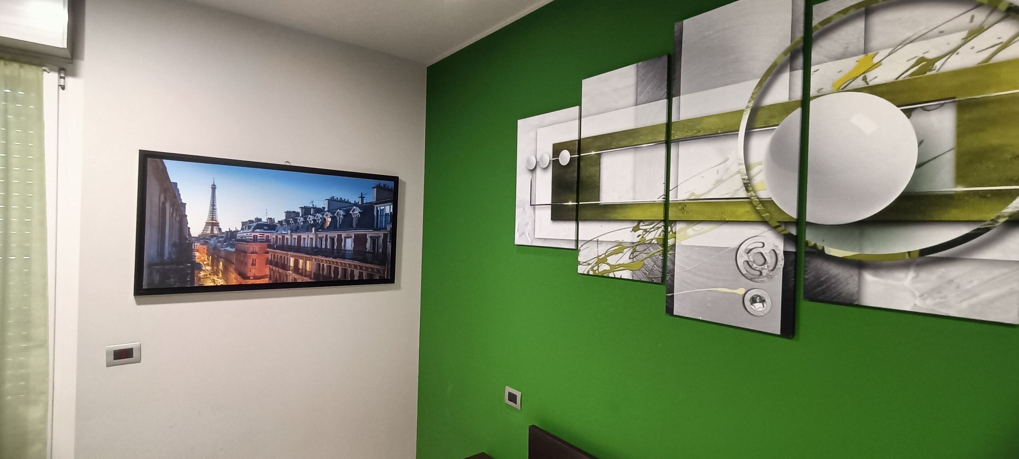 A room with a green accent wall, a framed picture of a cityscape, and abstract art.