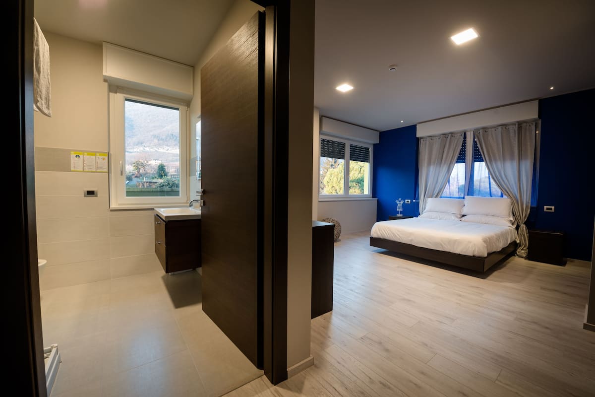 A modern bedroom with a large bed, a window with curtains, and a view of the outdoors.