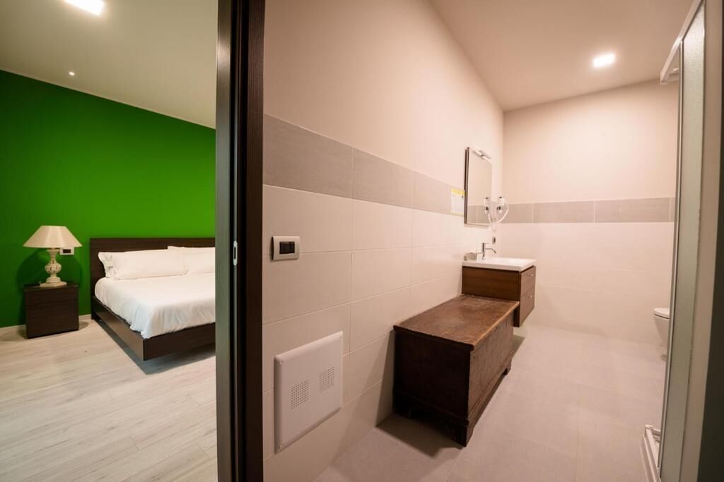A hotel room with a bed, bedside table, lamp, and a bathroom with a sink, mirror, and shower.
