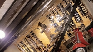 A restaurant with a wooden table set for dining, a red scooter, and a wall of wine bottles. - Millaenya Inn (Entratico)