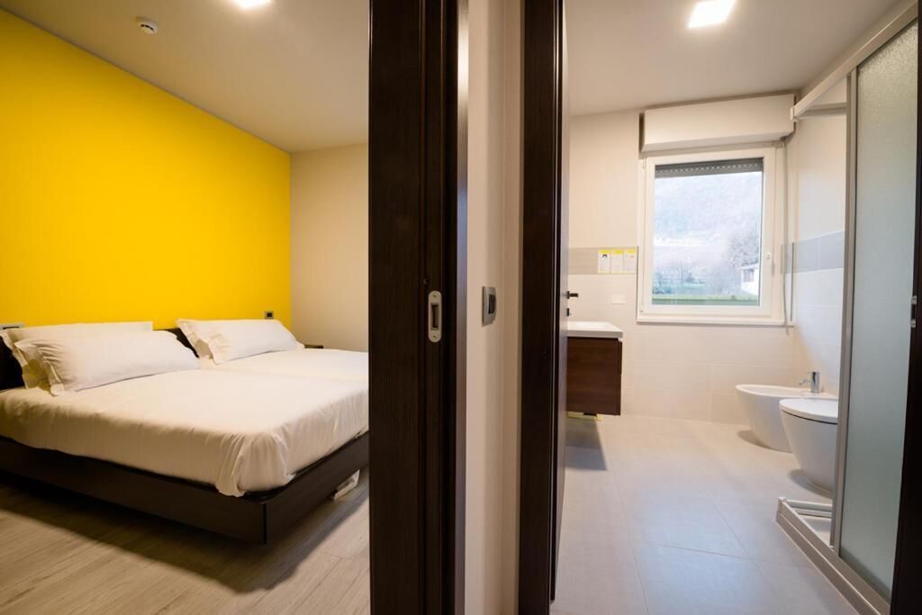 Un dormitorio moderno con una cama, una pared amarilla y un baño con inodoro y lavabo.
