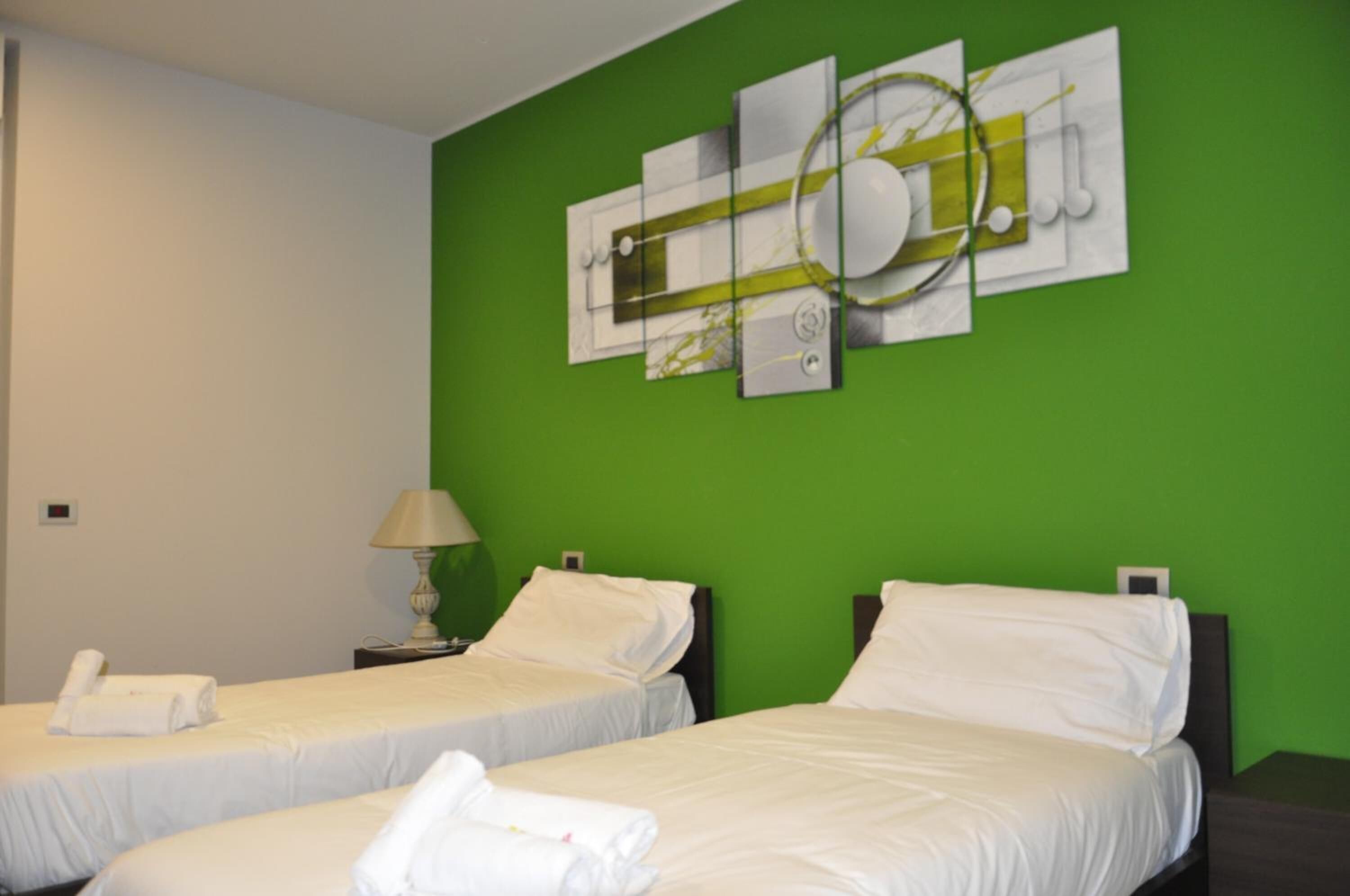 A hotel room with two beds, a green accent wall, and a modern abstract art piece above the beds.