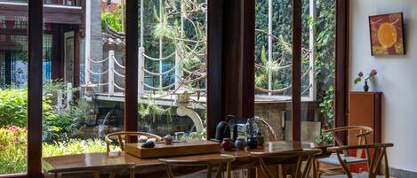 Un comedor con mesa y sillas de madera, ventanas amplias con vistas a zonas verdes y una fuente al exterior.