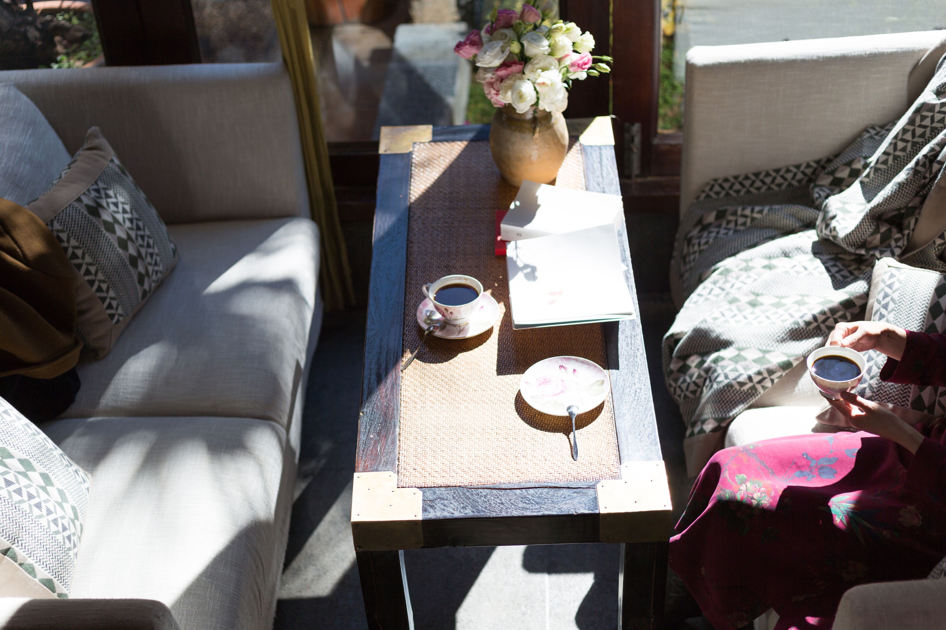 A seating area with a table, cushions, a vase with flowers, and a cup.