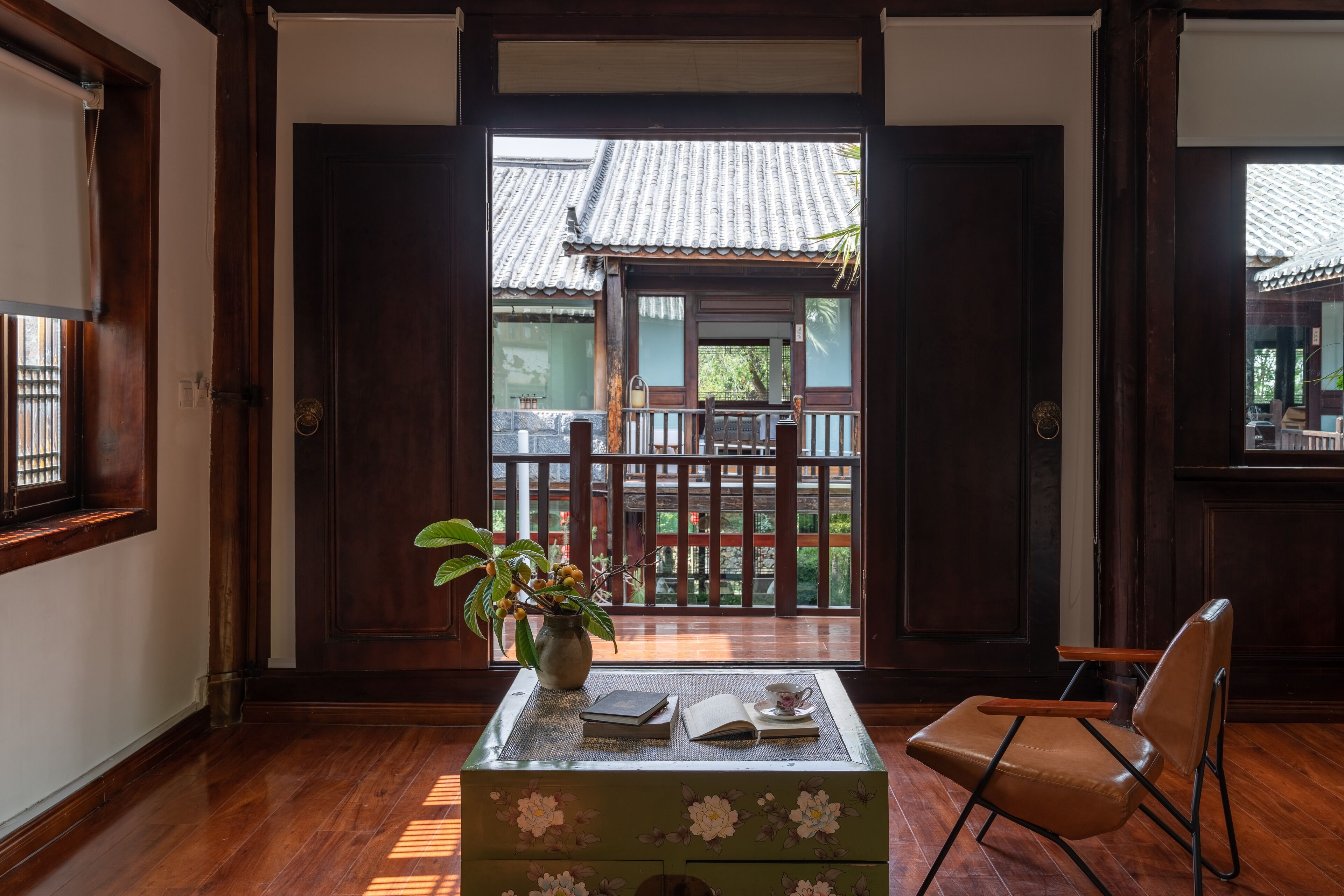 A traditional Japanese room with tatami flooring, a wooden desk with books and a vase, and a sliding door leading to a balcony with a tiled roof.