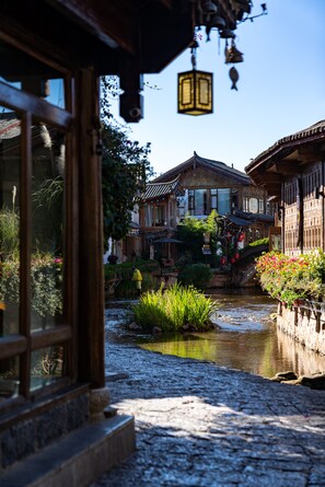 A traditional wooden building with a stone pathway leading to a small pond, surrounded by greenery and flowers. - Lijiang Hotel JunPoXuan (Lijiang)