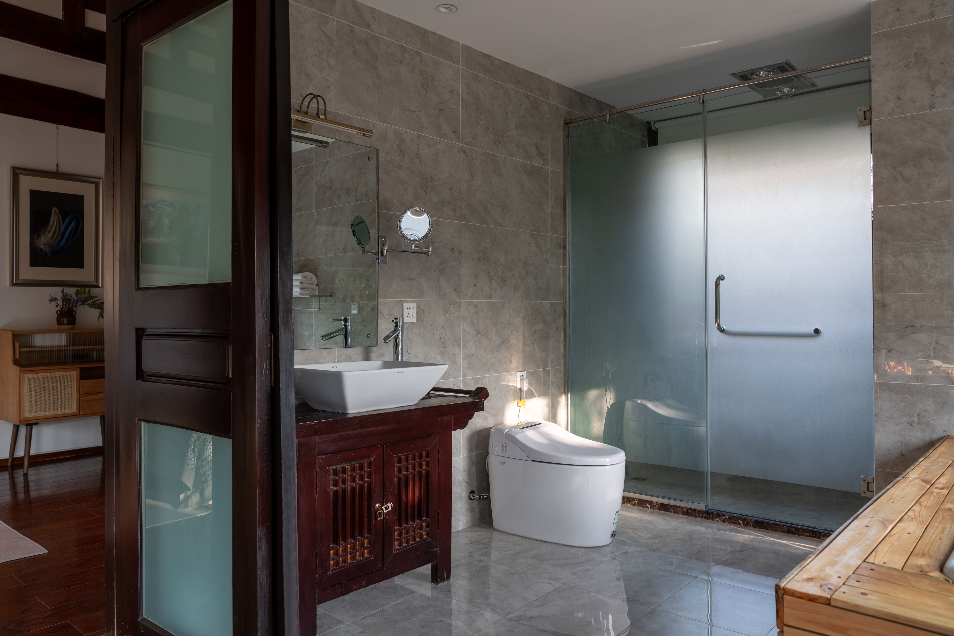 A modern bathroom with a glass shower enclosure, a wooden vanity, and a white toilet.