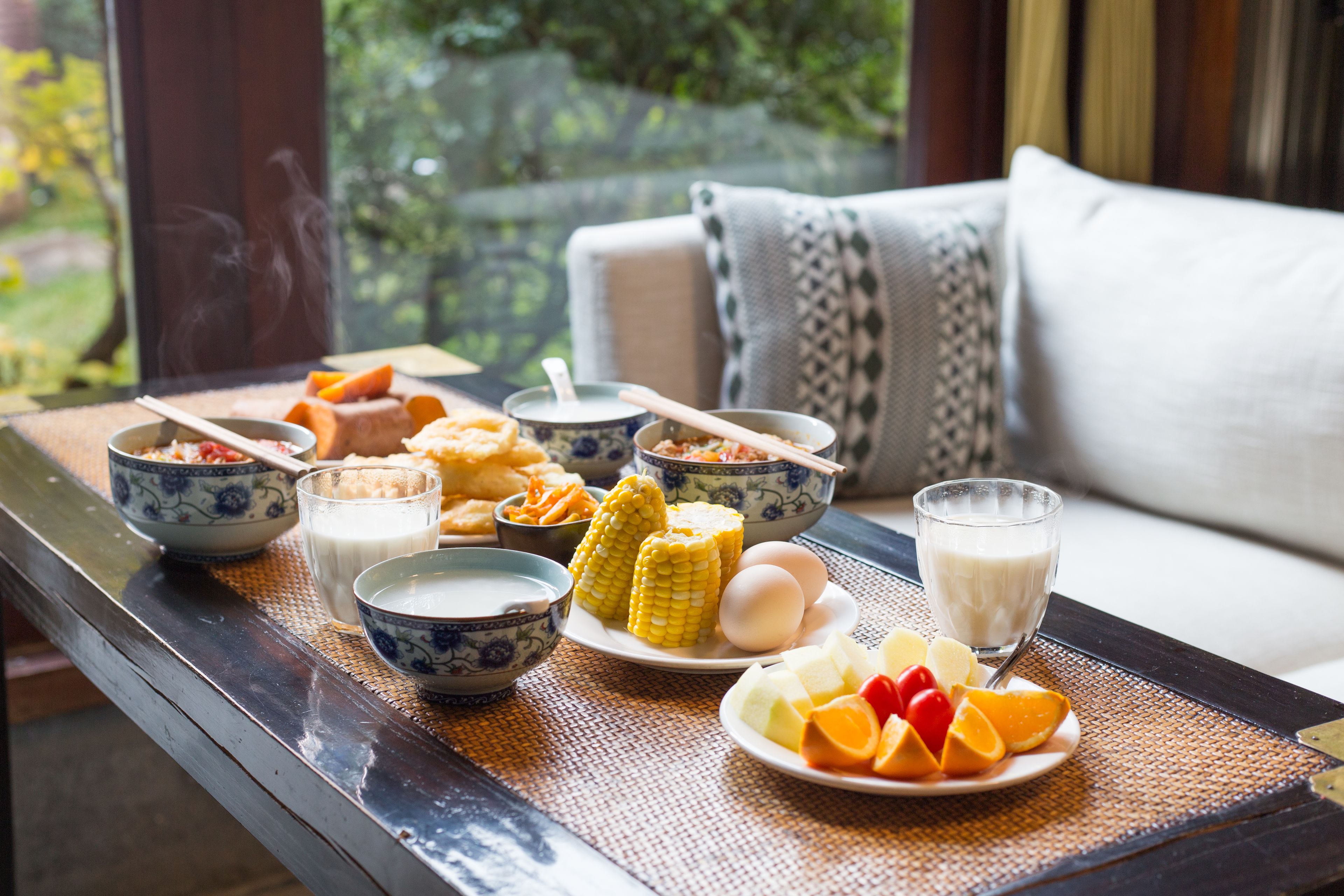 A breakfast tray with various foods and drinks on a table near a window.