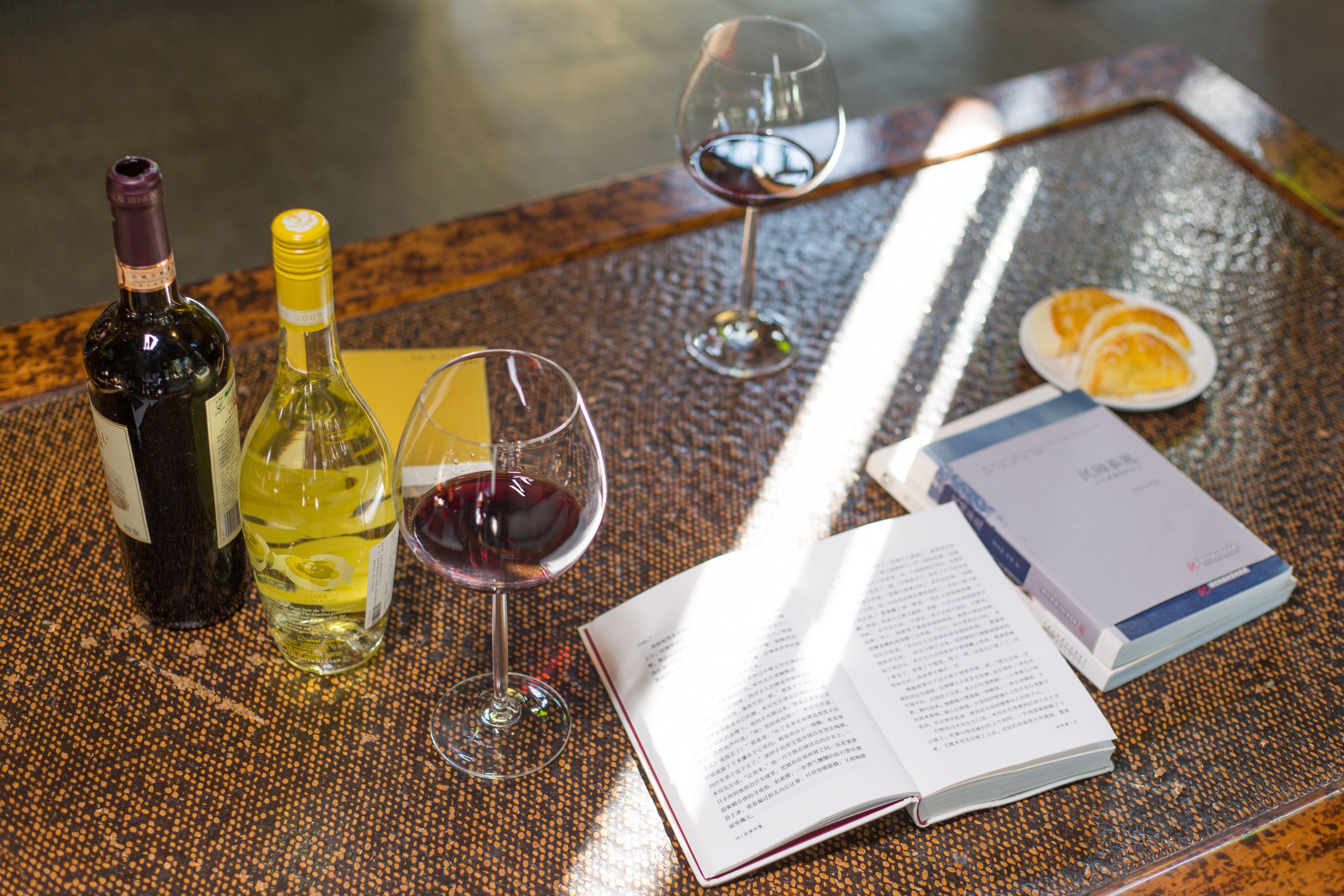 Une table avec un livre, deux bouteilles de vin, deux verres à vin et une assiette avec des tranches d’orange.