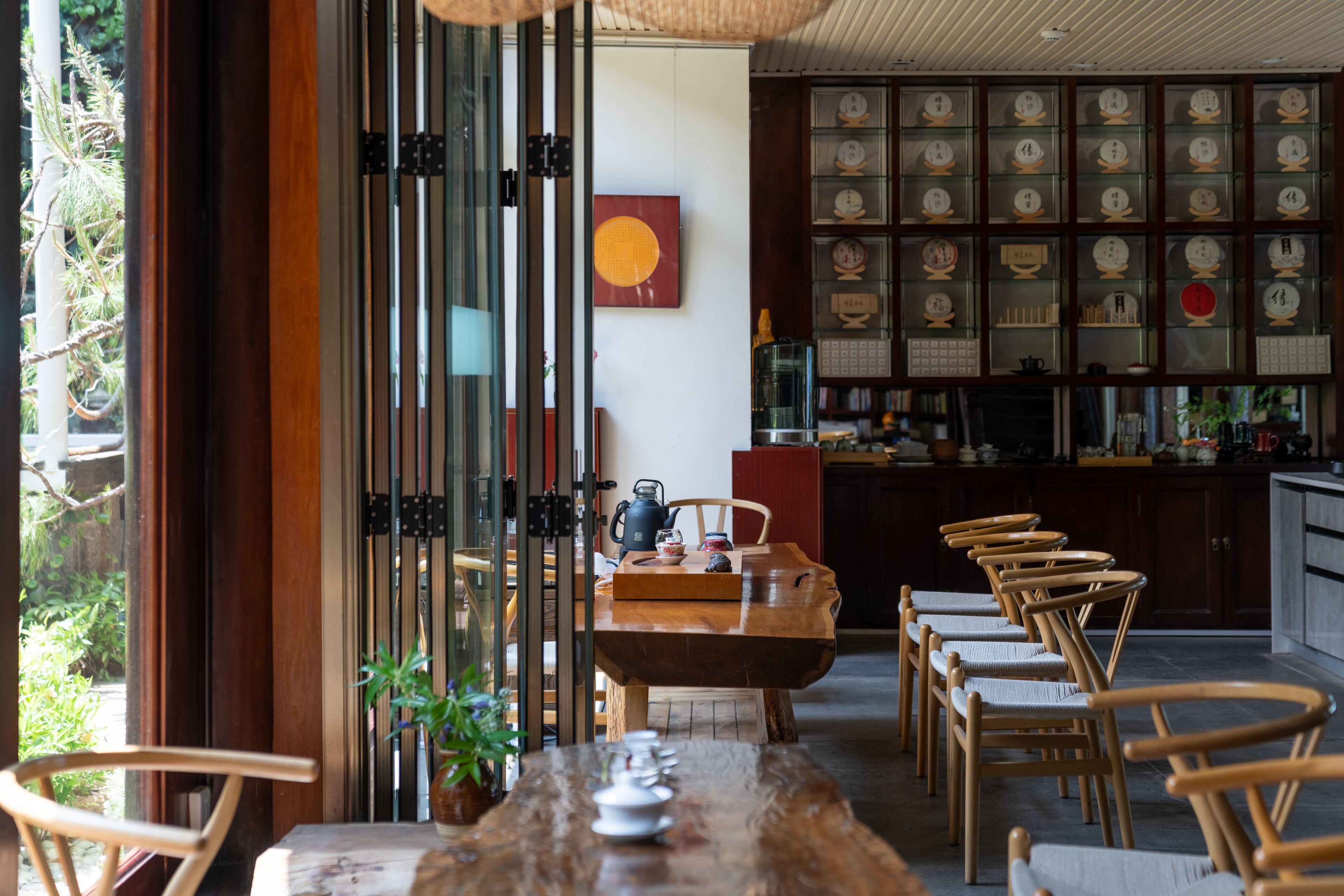 A wooden dining table with chairs, a glass partition, and a wall with clocks.