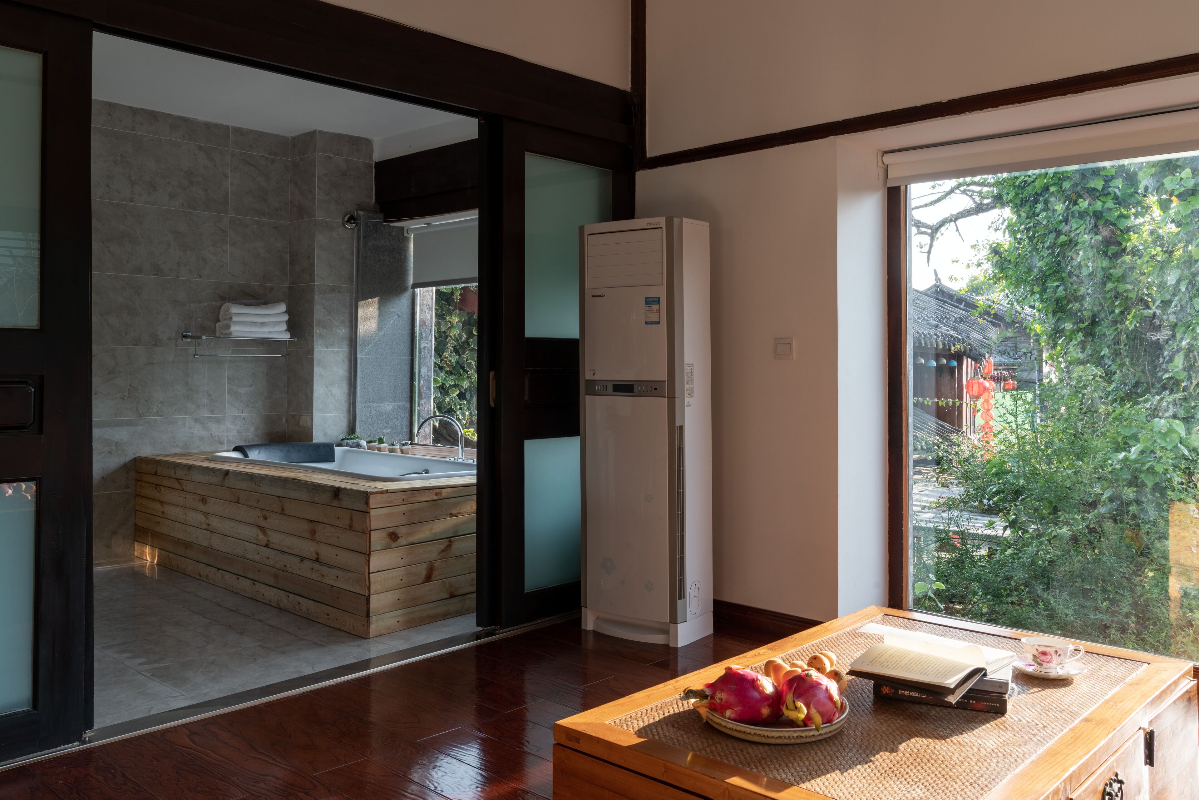Un bagno moderno con una vasca da bagno in legno, un water incassato e un'ampia finestra con vista sul verde.