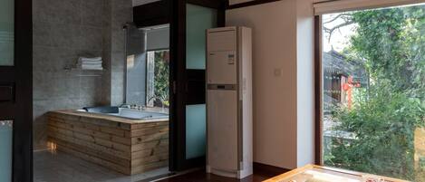 A modern bathroom with a wooden bathtub, a built-in toilet, and a large window offering a view of greenery.