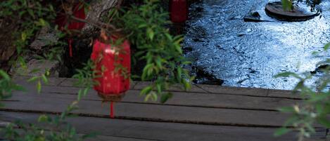 Un pont en bois enjambant un plan d’eau, avec des lanternes rouges suspendues à un arbre.