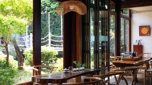 A wooden dining table with chairs, a hanging light fixture, and a view of a garden through large windows. - Lijiang Hotel JunPoXuan (Lijiang)