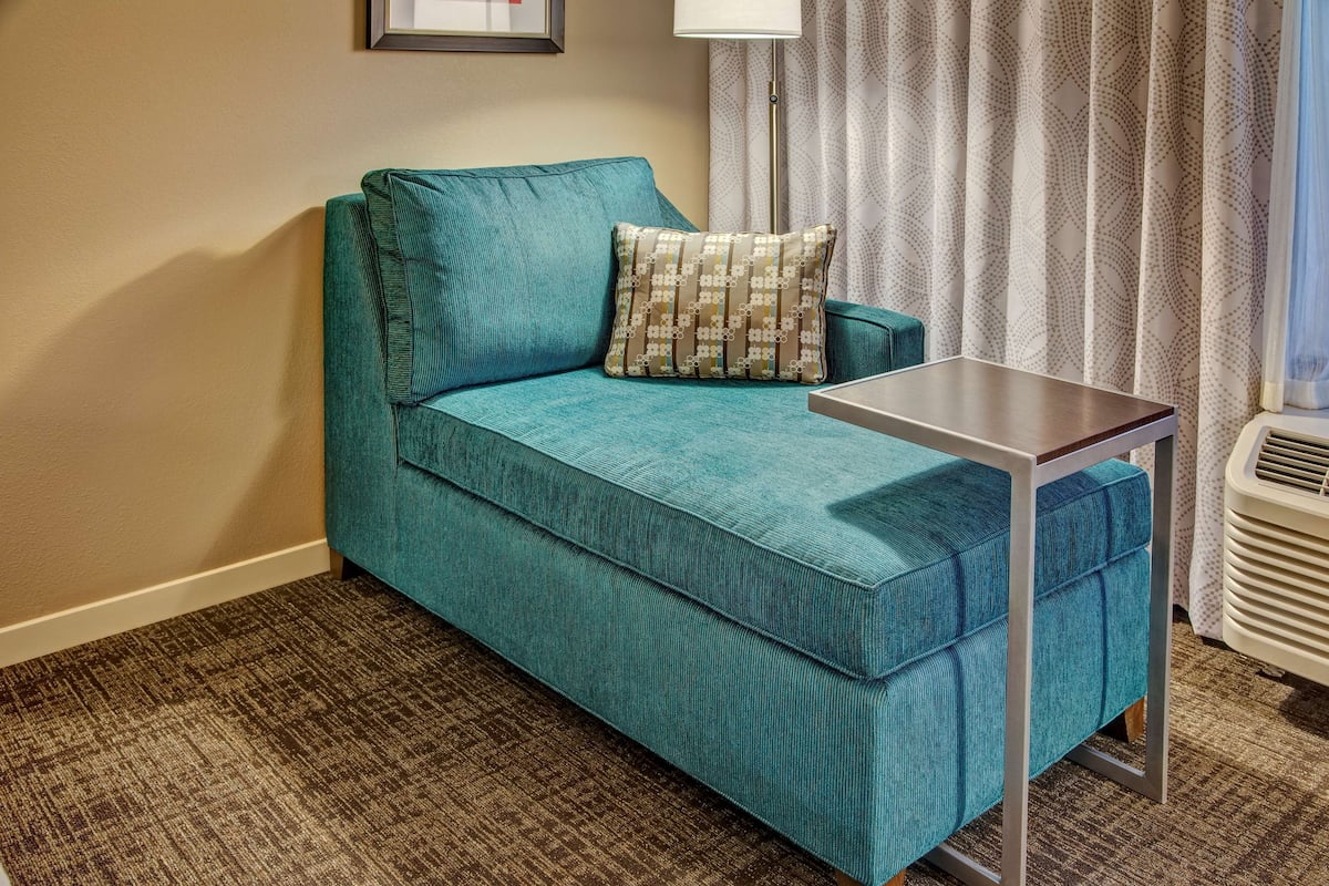 Un canapé de couleur turquoise orné d’un coussin à motifs, une petite table et un radiateur dans une chambre d’hôtel.