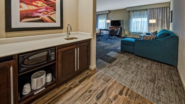 Une chambre d’hôtel avec une kitchenette, un coin salon doté d’un canapé et d’une télévision, et un tableau encadré au mur.