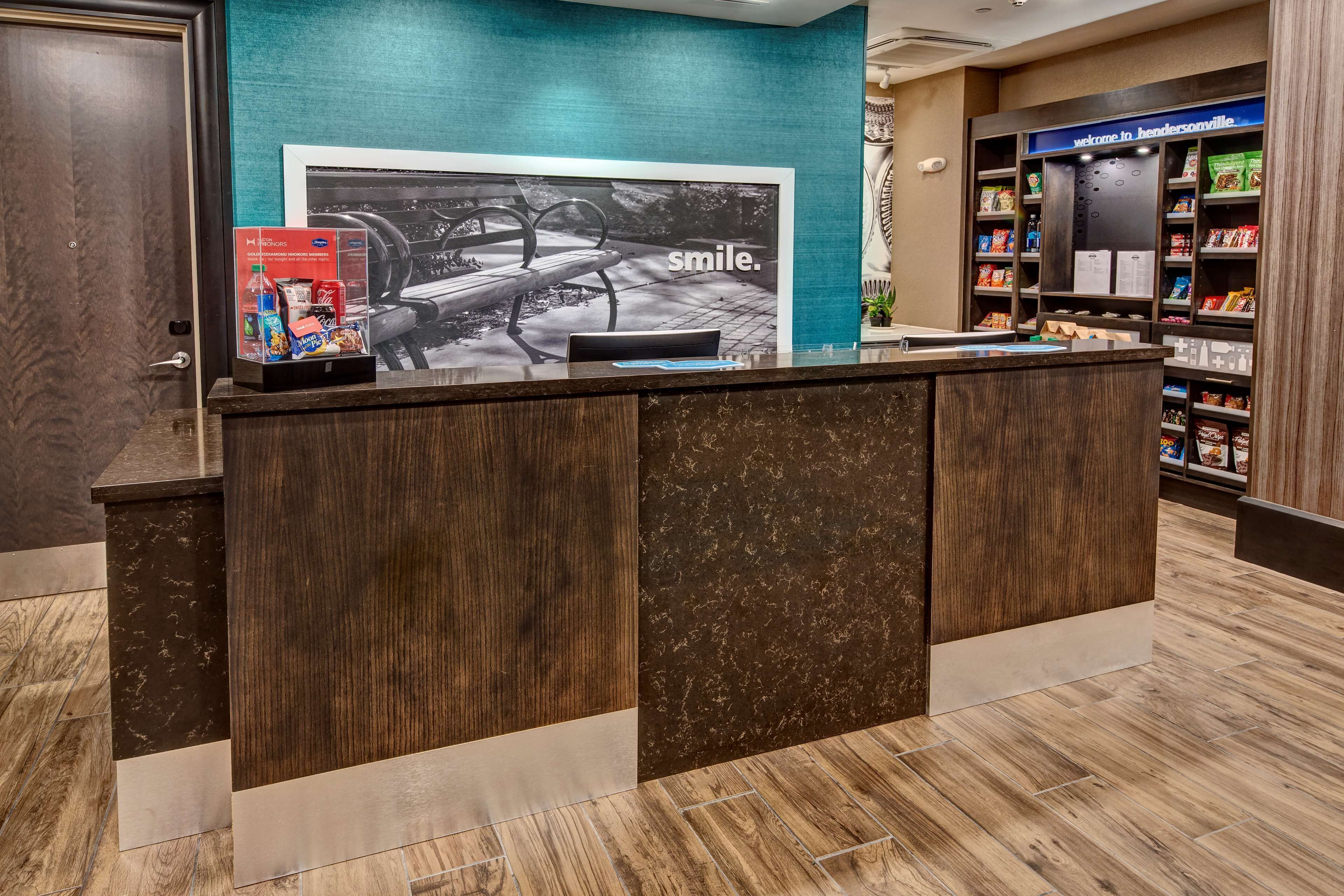 A reception desk with a 'smile' poster, a beverage dispenser, and a snack shelf.