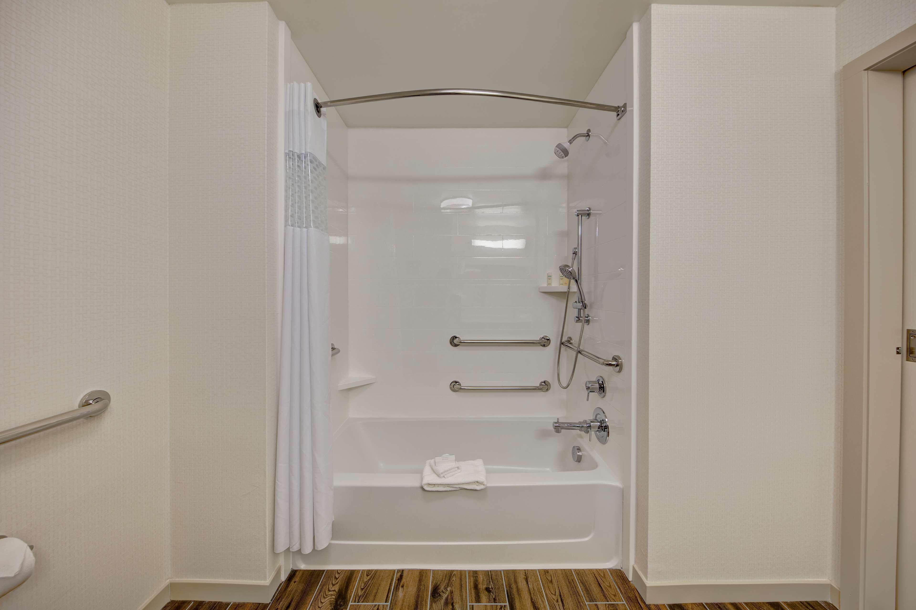 A bathroom with a bathtub, shower, and grab bars.
