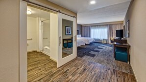 Une chambre d’hôtel avec un plancher en bois, un lit, un bureau, une télévision et une salle de bain équipée d’une douche et de toilettes.
