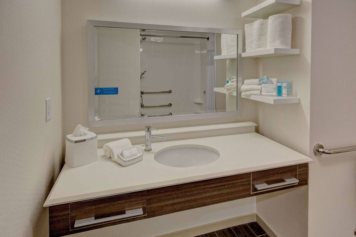 Une salle de bain équipée d’un lavabo, d’un miroir, d’un porte-serviettes et d’étagères de rangement.
