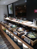 Un bufé con diversas opciones de comida, incluyendo platos vegetarianos, dispuesto sobre puestos de madera con etiquetas.